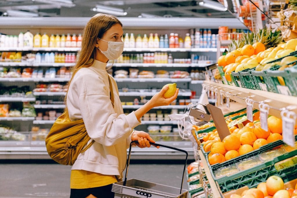 A masked woman shopping for produce during the COVID-19 pandemic. Retail and grocery consulting are of utmost importance during these uncertain times